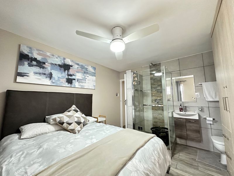 A modern bedroom featuring an integrated en-suite bathroom with a glass shower, stone-cladding detail, vanity basin, and built-in wardrobe storage.