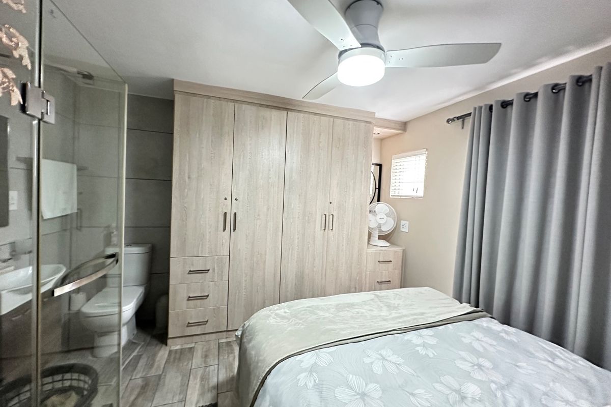 A well-maintained bedroom featuring built-in cupboards, a ceiling fan, and an en-suite bathroom with a glass shower enclosure.