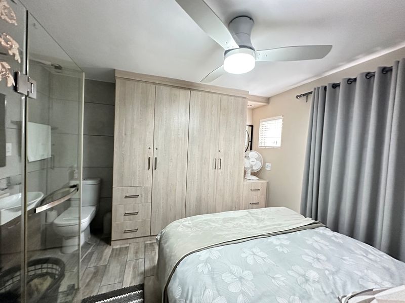 A well-maintained bedroom featuring built-in cupboards, a ceiling fan, and an en-suite bathroom with a glass shower enclosure.