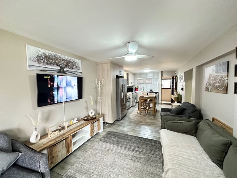 An open-plan living and kitchen area featuring tiled flooring, a ceiling fan, and a functional kitchen layout with built-in cabinetry and appliances.