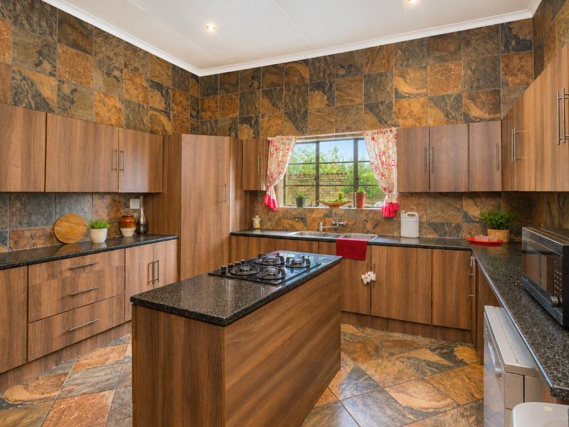 Spacious kitchen featuring wood-finish cabinetry, granite countertops, a central island with a gas hob, and distinctive slate wall and floor tiling.