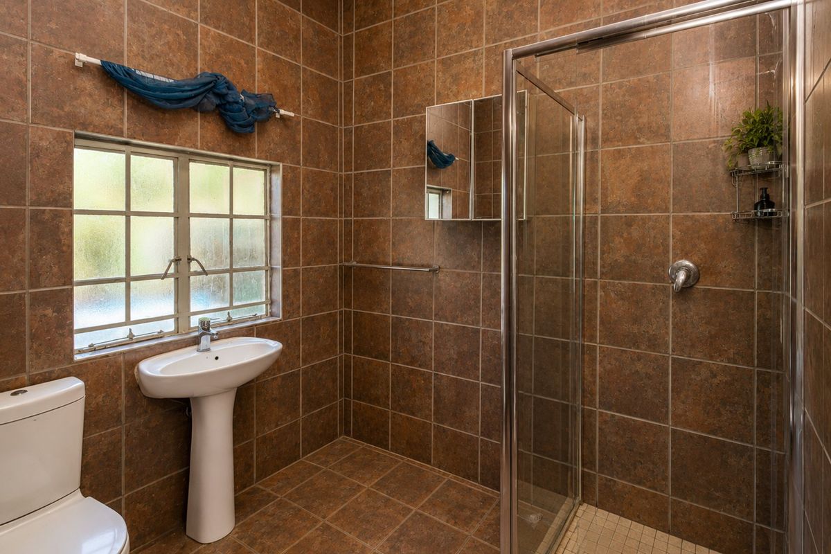 A functional bathroom featuring a pedestal basin, toilet, and a glass-enclosed shower, finished with full-height brown ceramic wall and floor tiles.