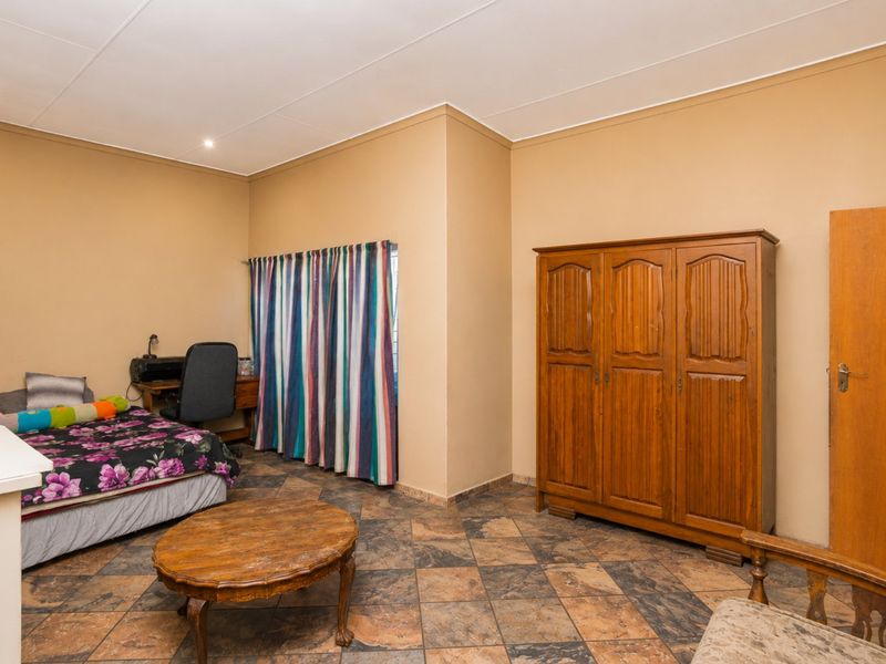 A spacious bedroom featuring tiled flooring, recessed ceiling lighting, and a solid wood door, offering a functional layout with neutral wall tones.