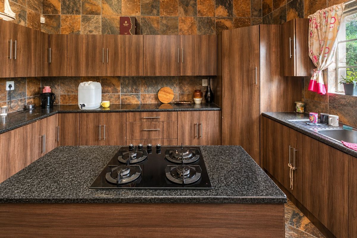 A functional kitchen featuring wood-finish cabinetry, dark granite countertops, a central island with a gas hob, and decorative stone-look wall tiling.