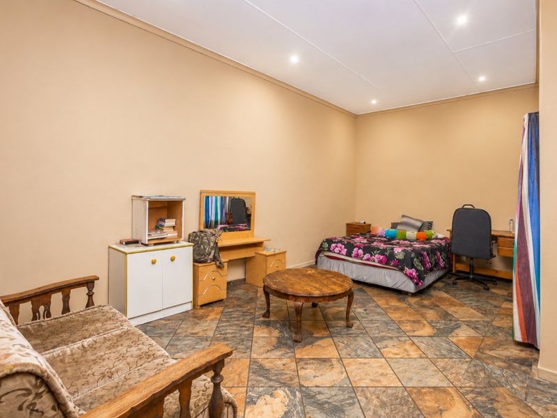 A spacious bedroom featuring tiled flooring and recessed downlighting, offering a neutral canvas for potential interior updates.