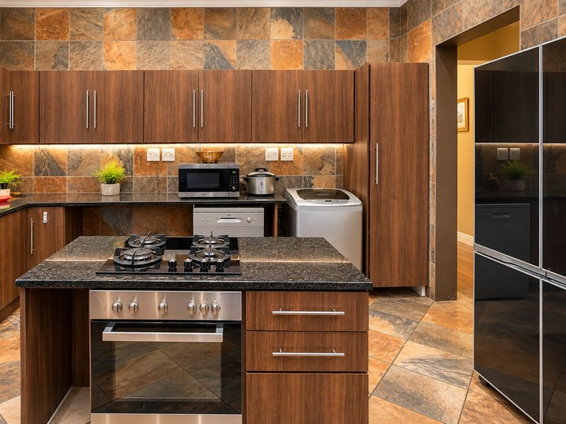 Modern kitchen featuring rich wood cabinetry, granite countertops, a central island with a gas hob and oven, and distinctive slate wall and floor tiling.