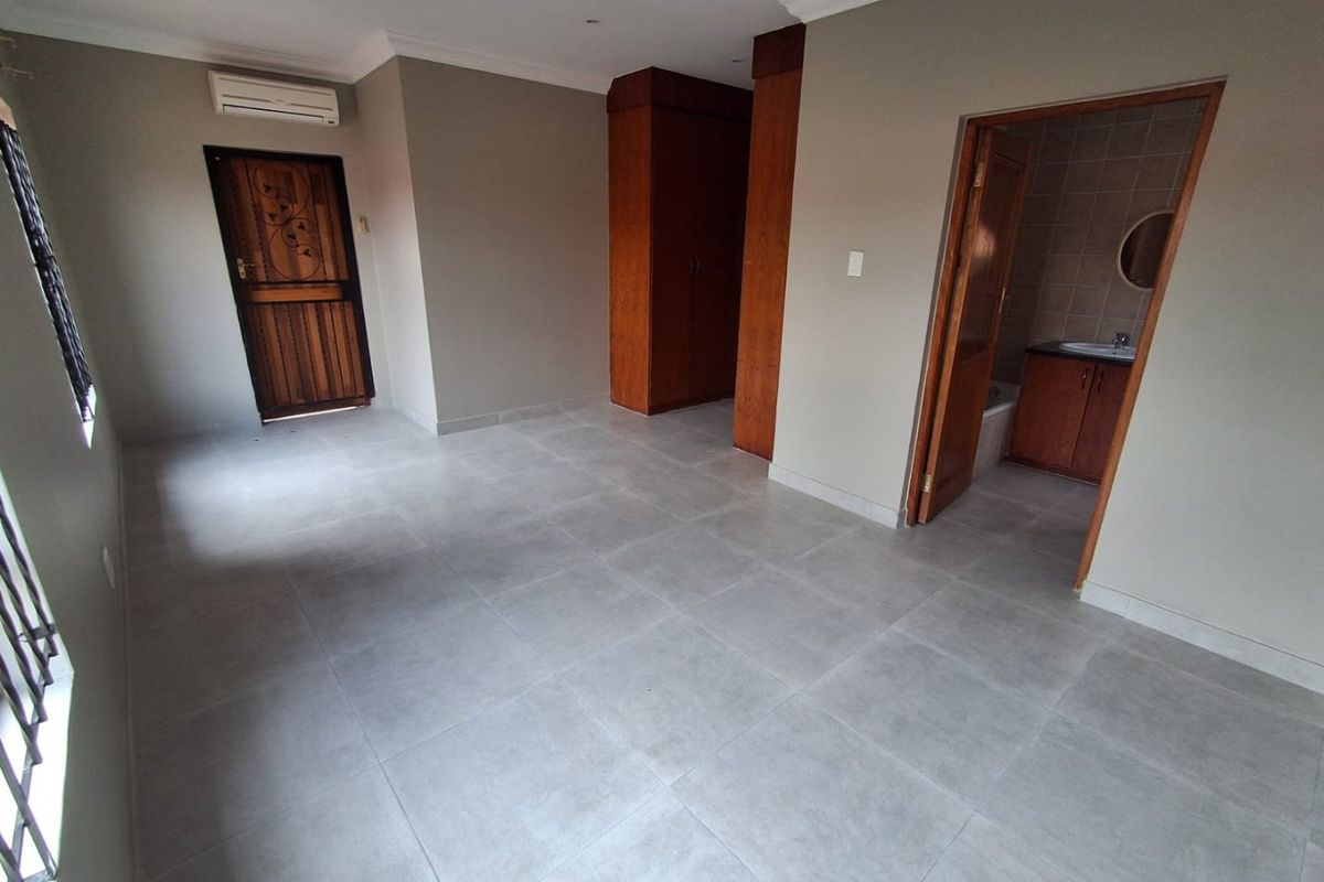 Spacious bedroom featuring neutral tiled flooring, built-in wooden cupboards, an air conditioning unit, and direct access to an en-suite bathroom.