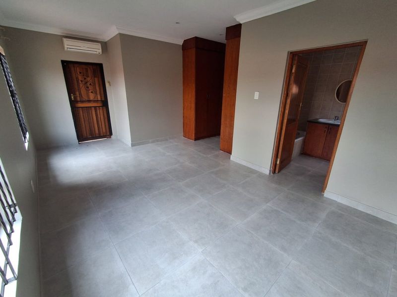 Spacious bedroom featuring neutral tiled flooring, built-in wooden cupboards, an air conditioning unit, and direct access to an en-suite bathroom.