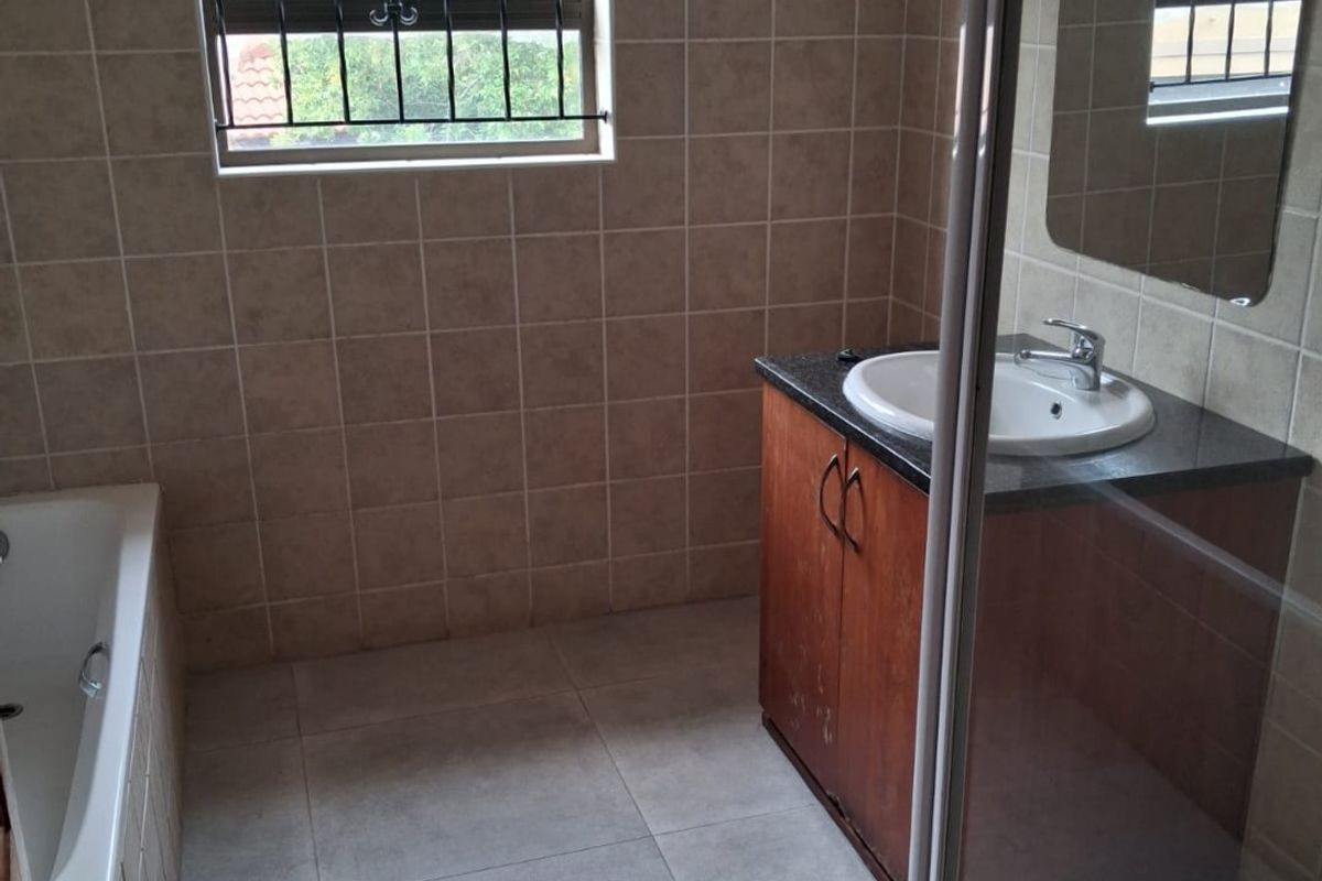 A functional bathroom featuring a built-in vanity, bathtub, and separate shower enclosure with tiled finishes and security bars on the window.