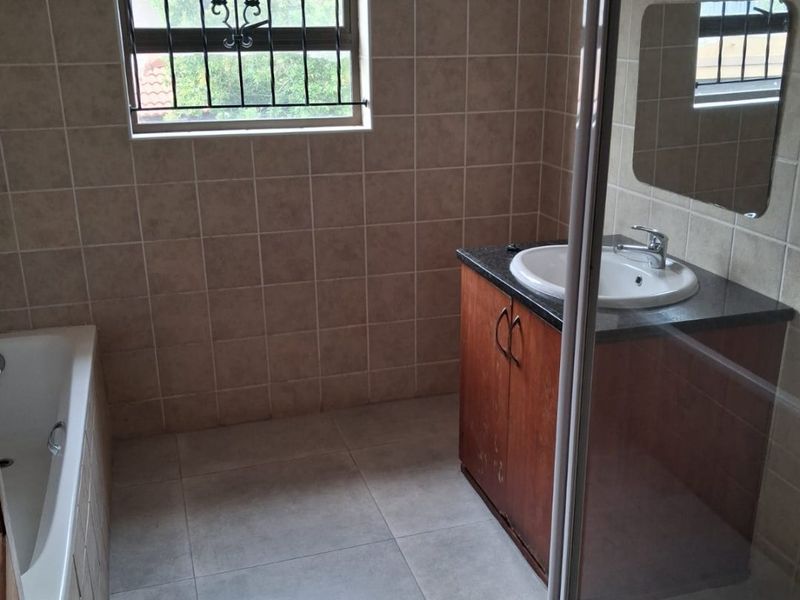 A functional bathroom featuring a built-in vanity, bathtub, and separate shower enclosure with tiled finishes and security bars on the window.