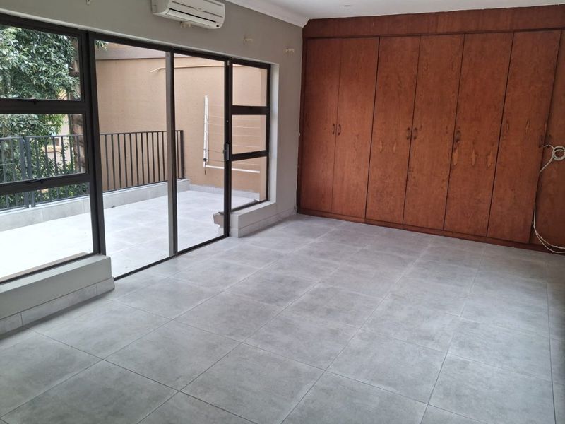 Spacious bedroom featuring large built-in wooden cupboards, modern grey tiled flooring, and direct access to a private balcony through sliding glass doors.