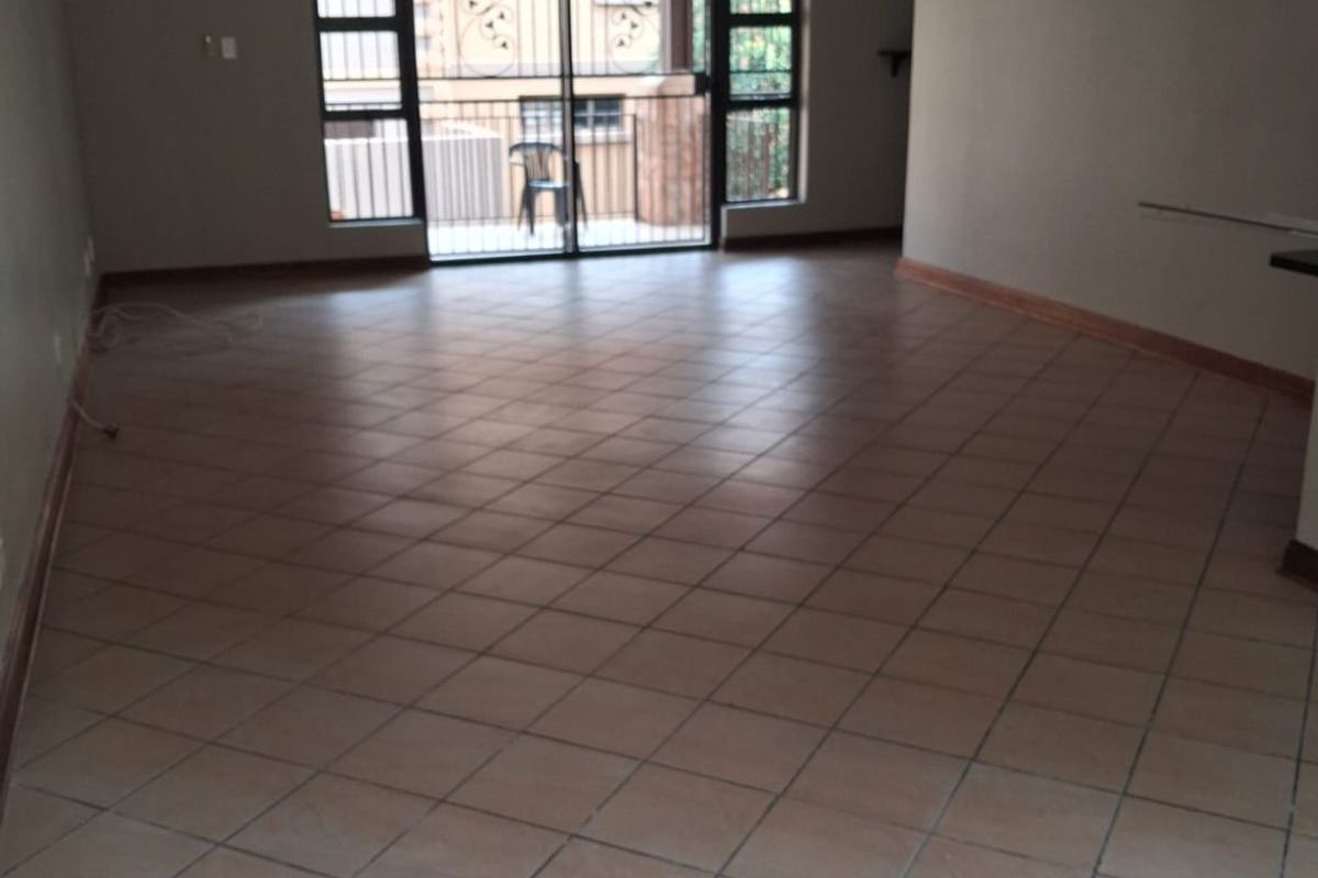 Spacious, empty living area featuring neutral tiled flooring, recessed lighting, and a sliding glass door with security gate leading to an outdoor space.