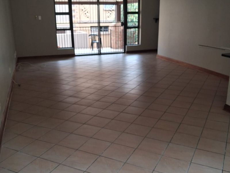 Spacious, empty living area featuring neutral tiled flooring, recessed lighting, and a sliding glass door with security gate leading to an outdoor space.