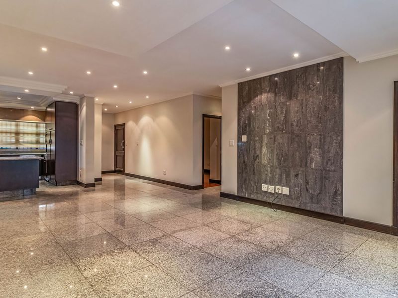 Spacious open-plan living area featuring polished granite flooring, a striking stone feature wall, recessed lighting, and an integrated kitchen with modern cabinetry.