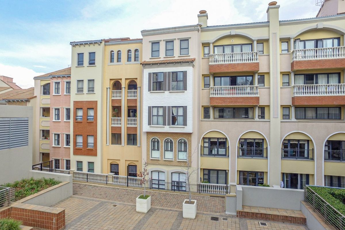 A view of the apartment complex rear facade featuring multi-level balconies, arched architectural detailing, and a paved courtyard area.