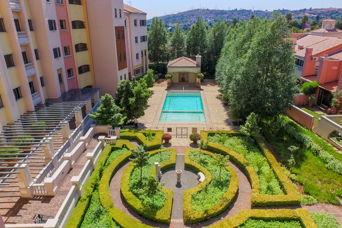 Aerial view of the apartment complex featuring a well-maintained swimming pool, landscaped garden with manicured hedges, and paved outdoor communal areas.