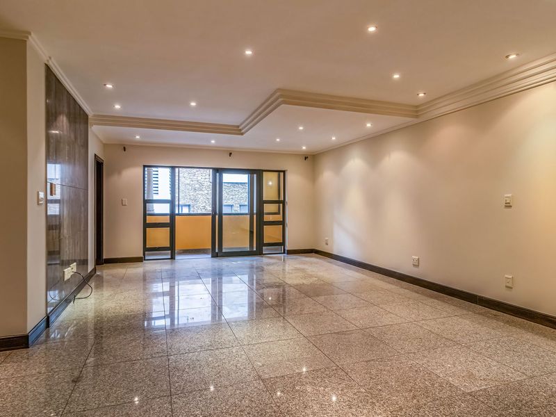 Spacious, empty living area featuring polished granite flooring, a coffered ceiling with recessed lighting, and a stone feature wall leading to a balcony.