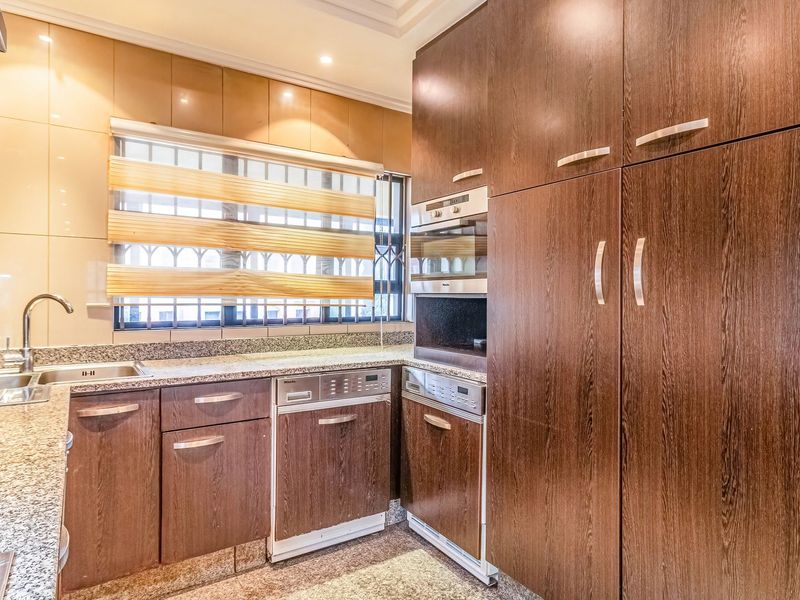 A well-maintained kitchen featuring dark wood cabinetry, granite countertops, integrated appliances, and a stainless steel sink with a modern mixer tap.