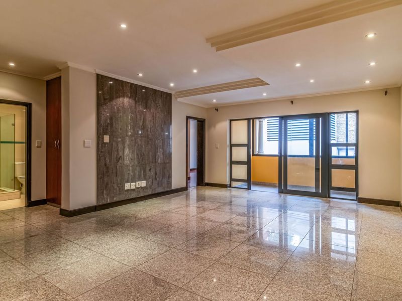 Spacious living area featuring polished granite flooring, a stone feature wall, recessed ceiling lighting, and direct access to a private balcony.