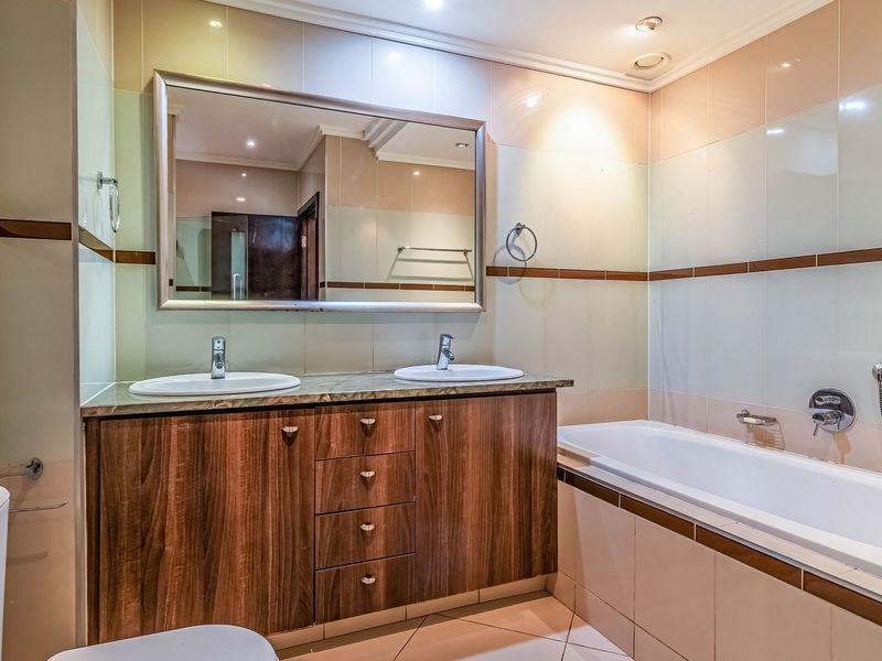 A well-maintained bathroom featuring a double vanity with wood-finish cabinetry, drop-in sinks, and a built-in bathtub with tiled surround.