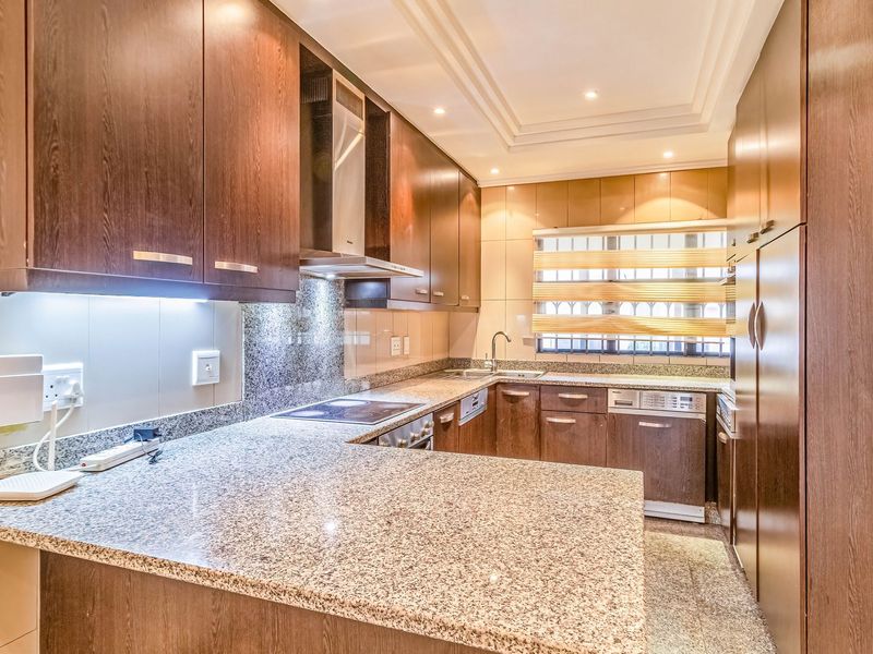 Modern kitchen featuring dark wood cabinetry, granite countertops, integrated appliances, and recessed lighting, offering a functional and well-maintained culinary space.