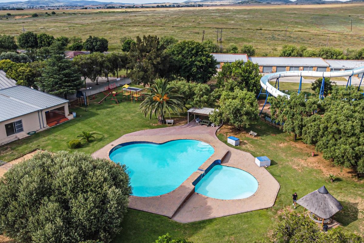 Aerial view of a property featuring a large swimming pool, water slide, landscaped garden, and a thatched gazebo in a rural setting.