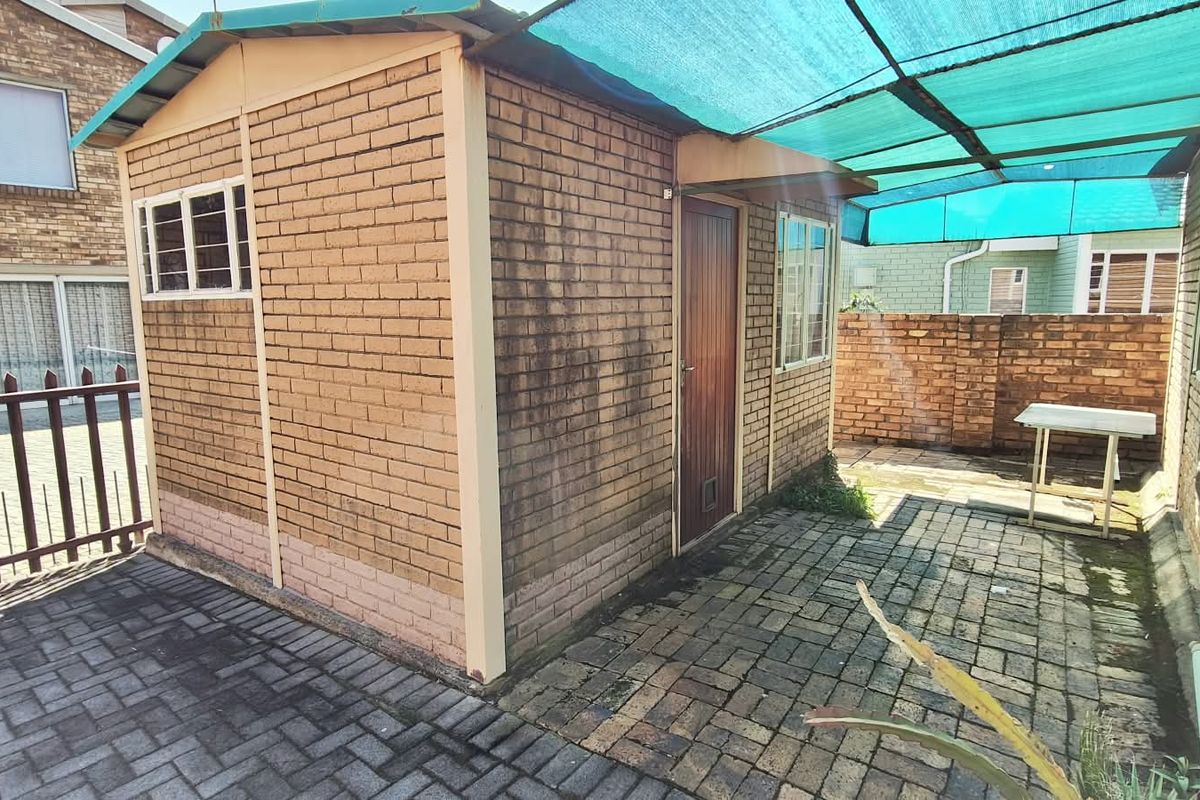 Rear exterior view of a brick outbuilding featuring paved flooring and a shade cloth canopy structure.