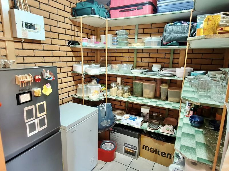 A functional scullery or pantry area featuring exposed brick walls, tiled flooring, and extensive built-in shelving for storage.