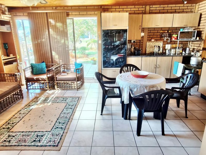Open-plan living and kitchen area featuring exposed brick walls, timber ceilings, tiled floors, and direct access to the outdoor patio through sliding glass doors.