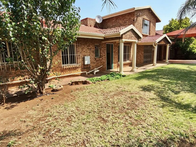 Rear view of a brick house featuring a covered patio area, security bars on windows, and a spacious garden with lawn.