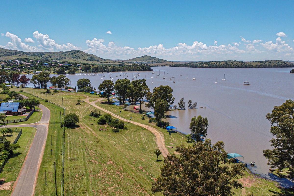 Aerial view of a scenic lakefront property featuring expansive green space, mature trees, and direct access to the water.