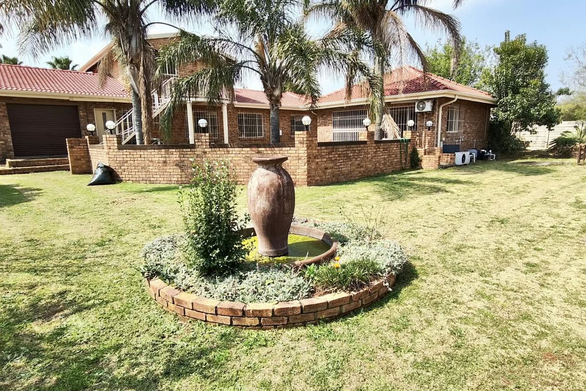 Rear view of a brick house featuring a landscaped garden with a central brick fountain, tiled roof, and secure perimeter walling.
