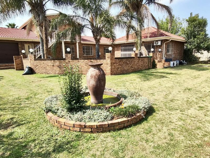 Rear view of a brick house featuring a landscaped garden with a central brick fountain, tiled roof, and secure perimeter walling.