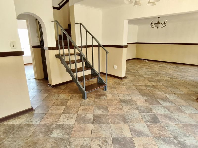 An open-plan living area featuring tiled flooring, a central staircase with a metal handrail, and decorative wainscoting throughout the space.