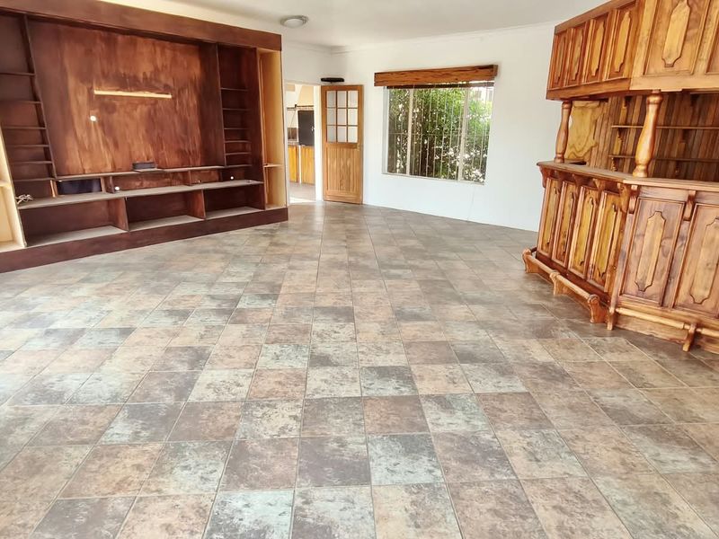 Spacious living area featuring a large built-in wooden shelving unit, a fixed wooden bar, and tiled flooring throughout.