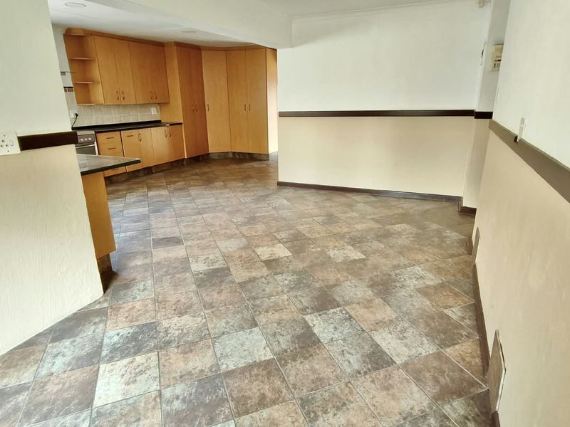 An open-plan living and kitchen area featuring dated wooden cabinetry, tiled flooring, and neutral wall finishes with decorative chair rail molding.