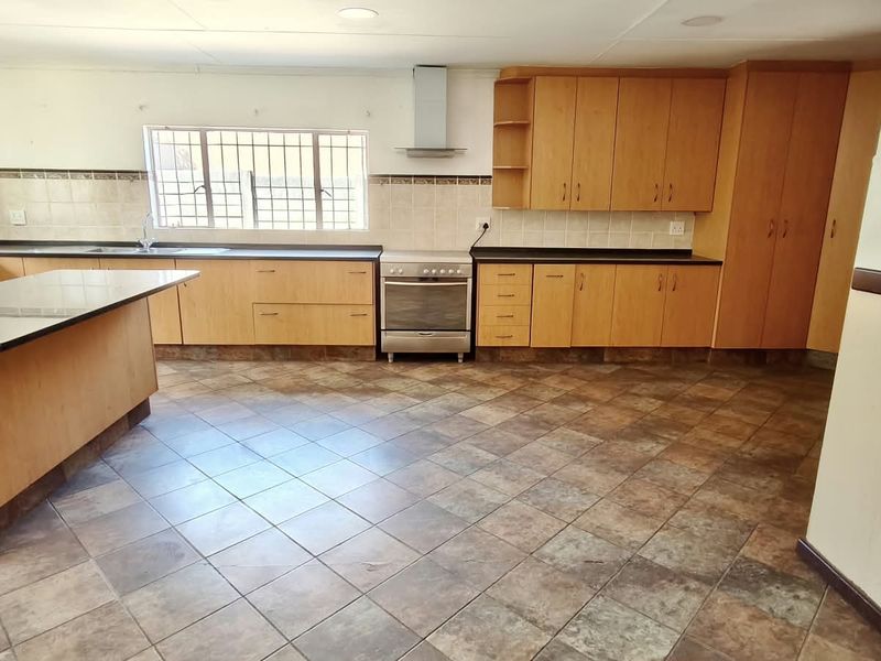 Spacious kitchen featuring extensive wooden cabinetry, dark laminate countertops, a stainless steel extractor fan, and tiled flooring throughout.