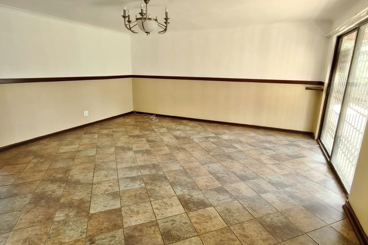 An empty living room featuring ceramic tile flooring, a decorative chandelier, and a sliding glass door with a security gate leading to the exterior.