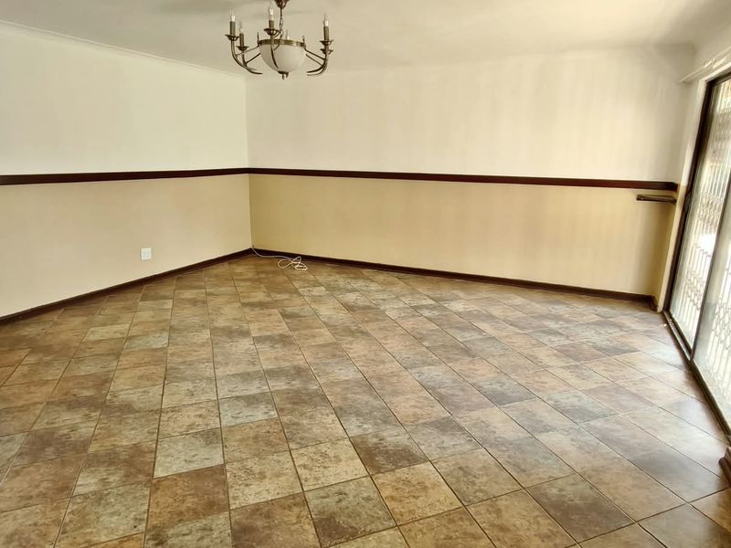 An empty living room featuring ceramic tile flooring, a decorative chandelier, and a sliding glass door with a security gate leading to the exterior.