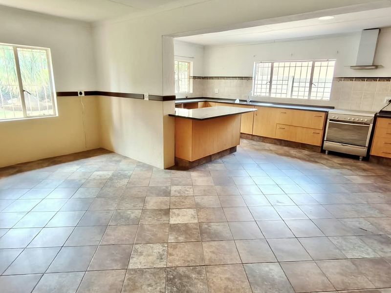 Spacious open-plan kitchen and living area featuring tiled flooring, built-in wooden cabinetry, and a functional kitchen island with a breakfast bar.