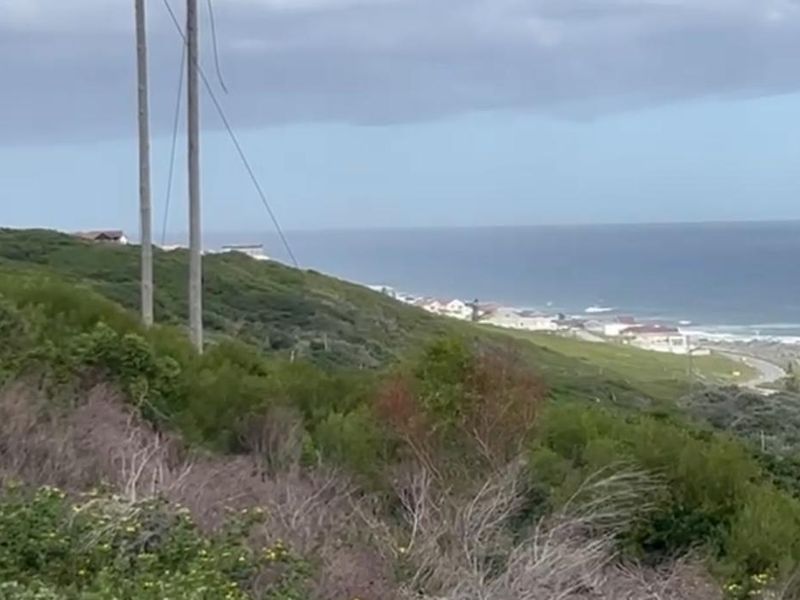 A scenic coastal landscape view overlooking the ocean and nearby residential properties, featuring natural vegetation and utility infrastructure.