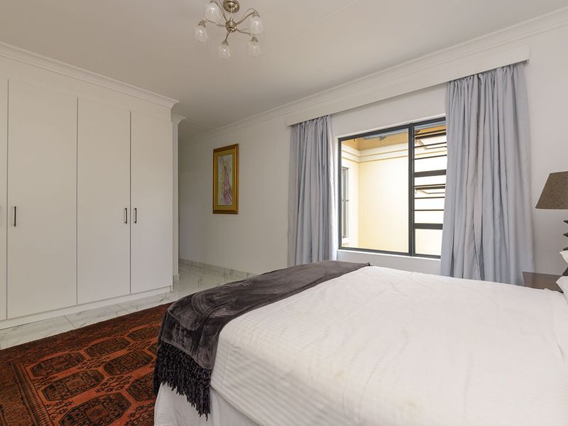 A well-maintained bedroom featuring built-in cupboards, marble-look floor tiles, and cove cornicing, offering a clean and neutral living space.