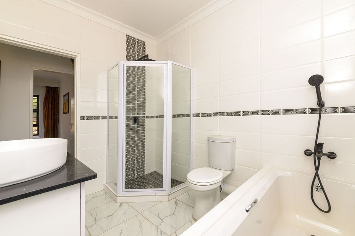 A clean, modern bathroom featuring a corner shower, built-in bathtub, toilet, and a vessel sink set on a vanity countertop with tiled finishes.