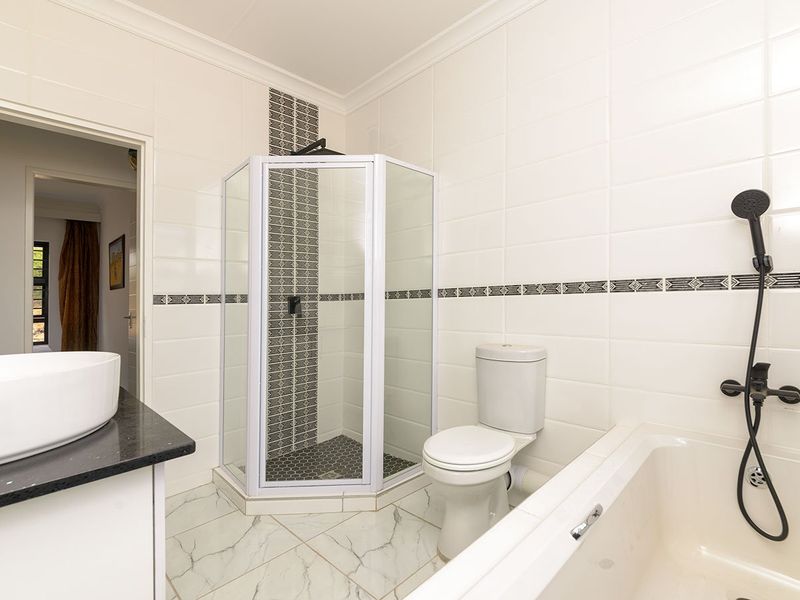 A clean, modern bathroom featuring a corner shower, built-in bathtub, toilet, and a vessel sink set on a vanity countertop with tiled finishes.