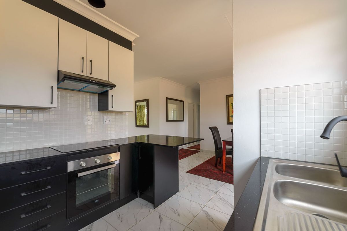 Modern kitchen featuring high-contrast black and white cabinetry, integrated appliances, tiled backsplash, and marble-look flooring, flowing into the adjacent dining area.