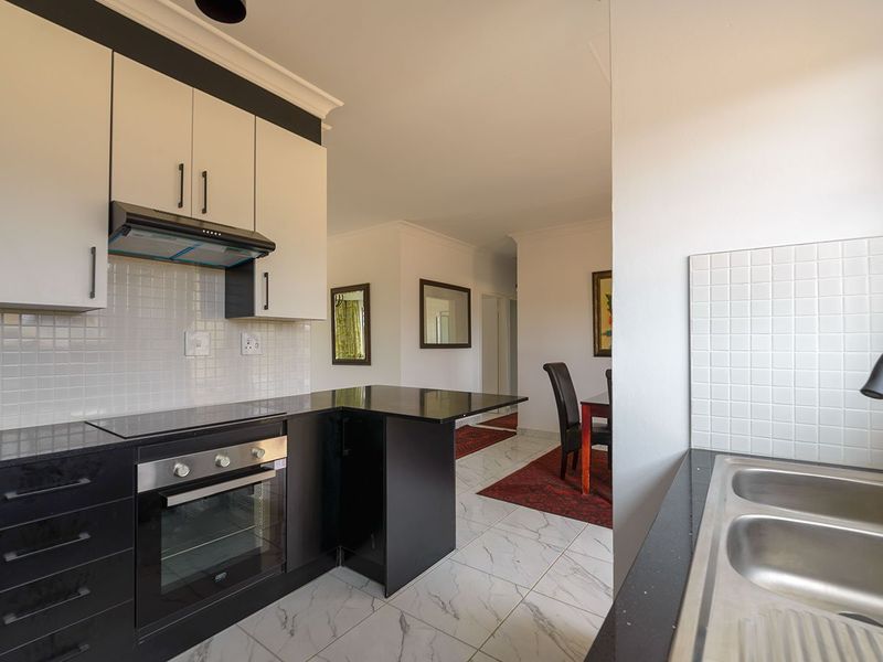 Modern kitchen featuring high-contrast black and white cabinetry, integrated appliances, tiled backsplash, and marble-look flooring, flowing into the adjacent dining area.