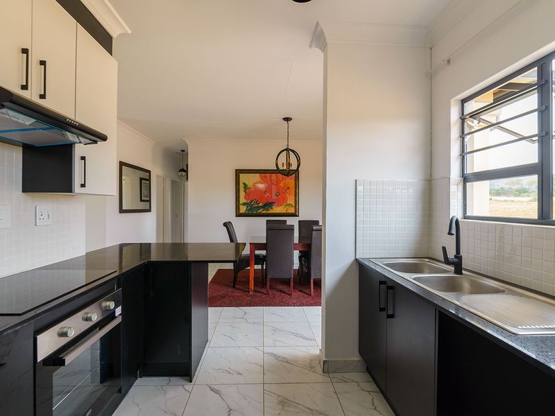 Modern open-plan kitchen featuring sleek black cabinetry, granite countertops, built-in oven, and a double sink, flowing seamlessly into the adjacent dining area.