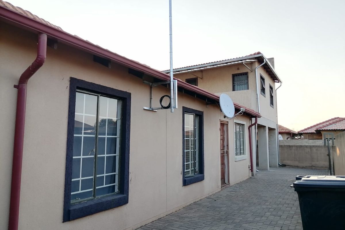 Rear exterior view of the house featuring a paved driveway, tiled roof, and security bars on the windows.