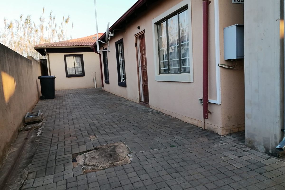 Rear exterior view of the property featuring paved ground, security gate, and boundary walling.