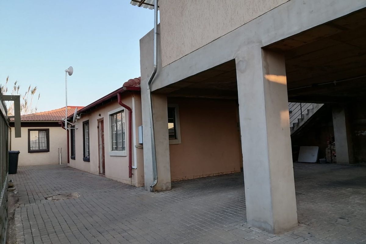 Rear exterior view of the property featuring a paved driveway, covered parking area with concrete pillars, and an external staircase.
